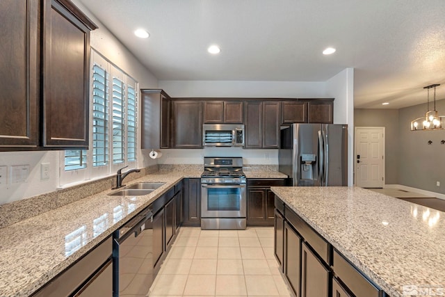 kitchen with dark brown cabinetry, appliances with stainless steel finishes, light stone counters, and a sink