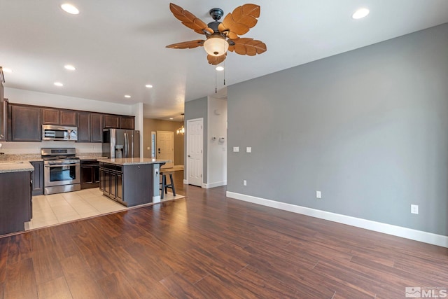 kitchen with dark brown cabinetry, a ceiling fan, light wood-style flooring, appliances with stainless steel finishes, and a center island