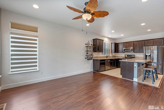 kitchen featuring appliances with stainless steel finishes, a kitchen breakfast bar, a center island, dark brown cabinets, and light wood-type flooring