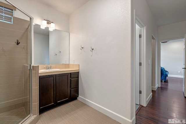 full bath featuring a stall shower, vanity, baseboards, and wood finished floors