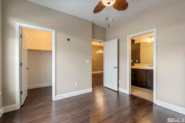 unfurnished bedroom featuring ensuite bathroom, dark wood-style flooring, a sink, baseboards, and a walk in closet