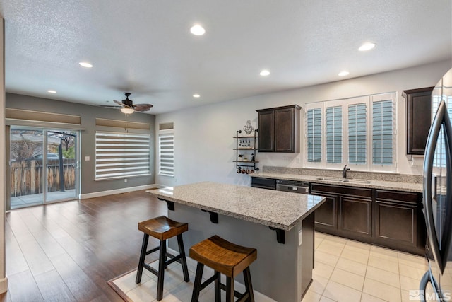 kitchen with a center island, a breakfast bar area, stainless steel appliances, a sink, and dark brown cabinetry