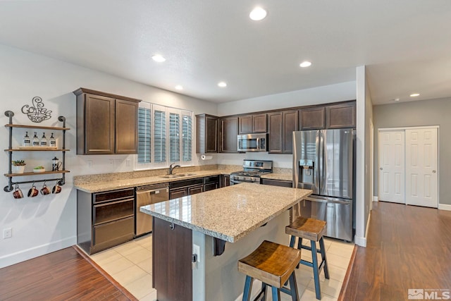 kitchen featuring stainless steel appliances, light wood-style flooring, dark brown cabinetry, and light stone countertops