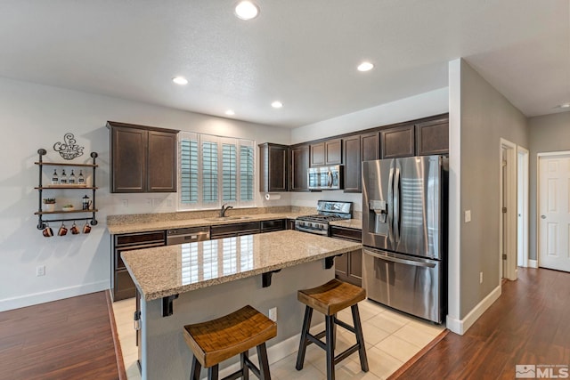 kitchen featuring a kitchen island, a sink, dark brown cabinets, appliances with stainless steel finishes, and light wood-type flooring