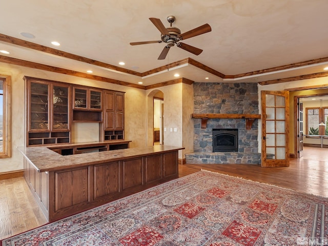 kitchen featuring light wood finished floors, arched walkways, ceiling fan, glass insert cabinets, and a fireplace