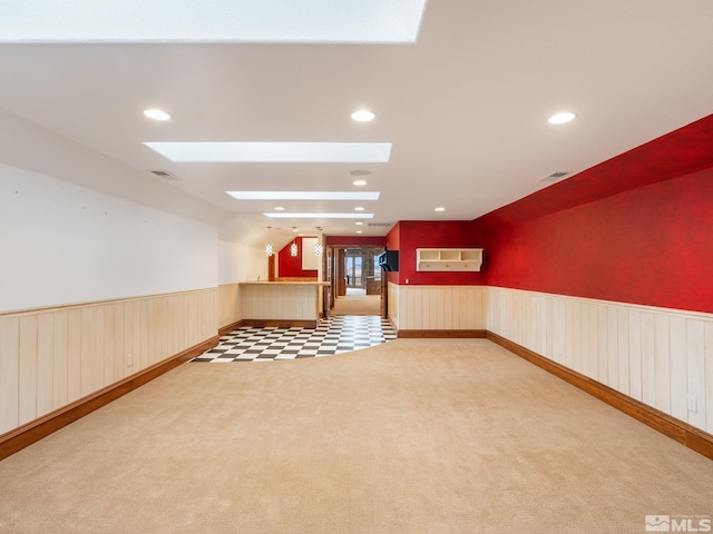 carpeted empty room featuring lofted ceiling with skylight, wainscoting, visible vents, and recessed lighting