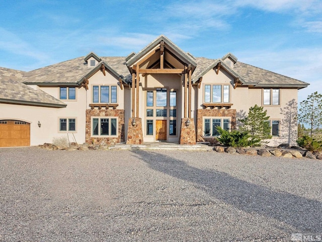 view of front of home with a garage, stone siding, and stucco siding