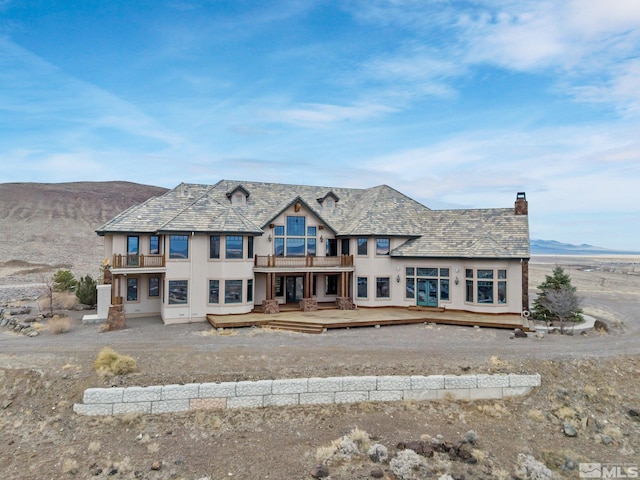 rear view of house featuring a chimney, a mountain view, a balcony, and stucco siding