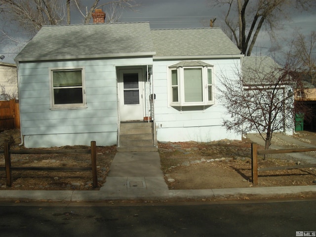 view of front of property with roof with shingles, a chimney, and fence