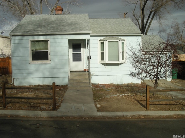 view of front of home featuring entry steps, a shingled roof, a chimney, and fence