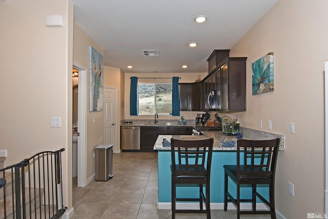 kitchen featuring stainless steel appliances, visible vents, dark brown cabinets, light stone countertops, and a peninsula