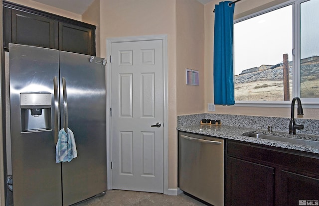 kitchen featuring appliances with stainless steel finishes, a sink, dark brown cabinetry, and light stone countertops