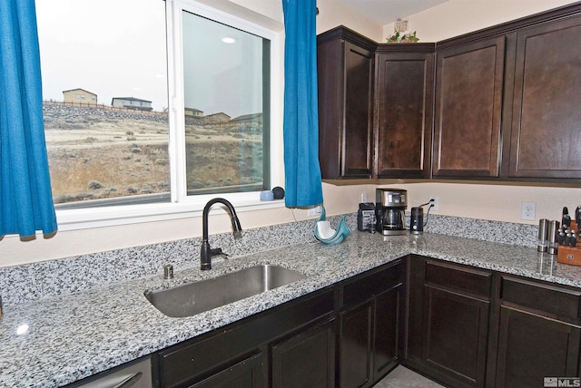 kitchen with light stone countertops, dark brown cabinets, and a sink