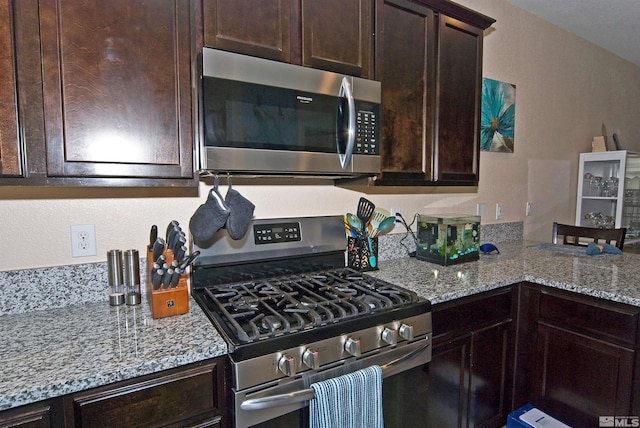 kitchen with light stone countertops, dark brown cabinetry, and appliances with stainless steel finishes