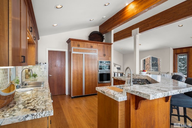 kitchen with double oven, brown cabinetry, paneled fridge, and a sink