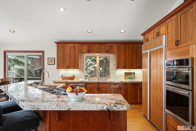 kitchen with stainless steel double oven, paneled built in refrigerator, light wood-type flooring, backsplash, and brown cabinets