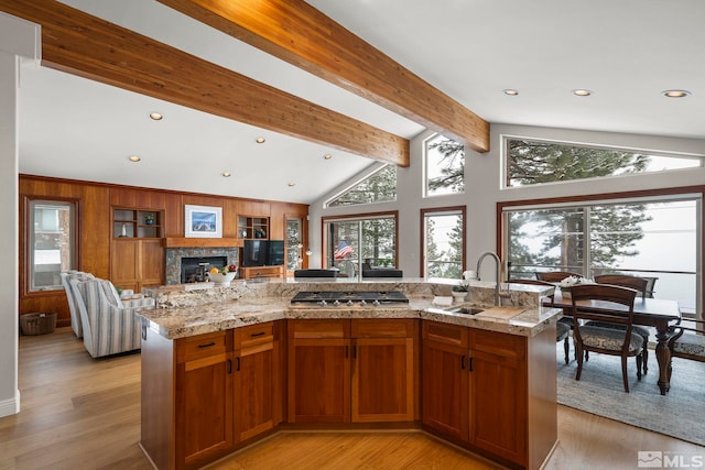 kitchen with open floor plan, lofted ceiling with beams, light wood-type flooring, and a sink