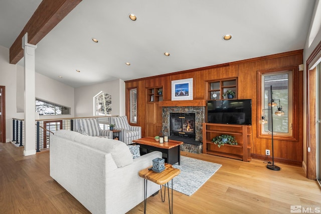 living area with a glass covered fireplace, beamed ceiling, wooden walls, and light wood finished floors