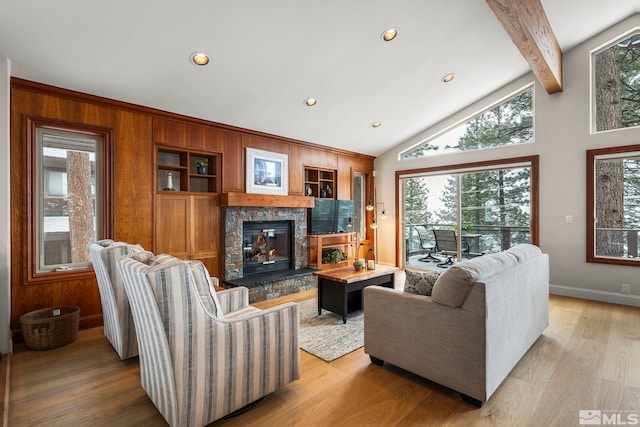 living area with built in features, light wood finished floors, recessed lighting, lofted ceiling with beams, and a glass covered fireplace