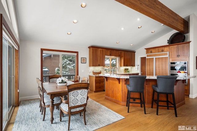 kitchen with lofted ceiling with beams, brown cabinetry, a sink, and paneled built in fridge