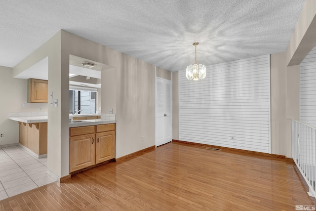 unfurnished dining area featuring a textured ceiling, light wood-type flooring, visible vents, and an inviting chandelier