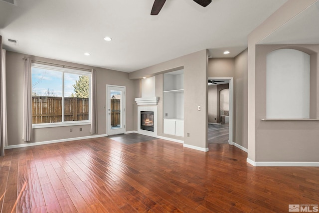 unfurnished living room with a glass covered fireplace, baseboards, visible vents, and wood-type flooring