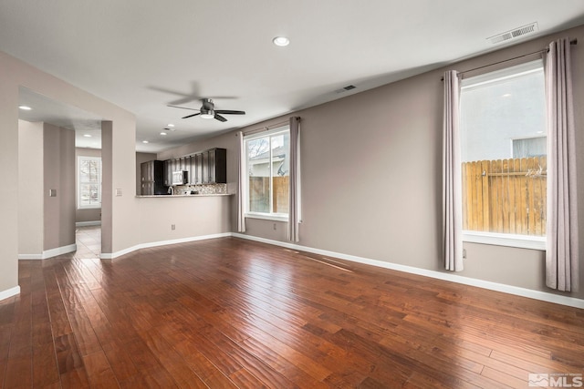 unfurnished living room with a wealth of natural light, visible vents, and dark wood-type flooring