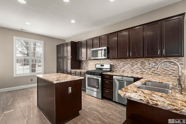 kitchen featuring dark brown cabinets, a center island, light stone counters, stainless steel appliances, and a sink