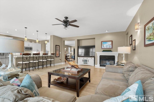 living room with recessed lighting, light wood-style floors, a glass covered fireplace, a ceiling fan, and baseboards