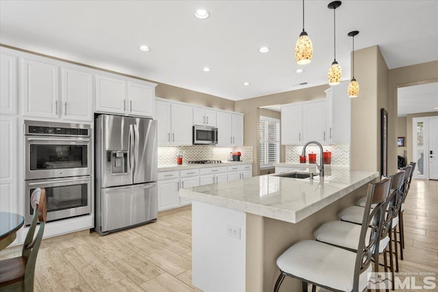 kitchen featuring stainless steel appliances, white cabinets, a sink, a peninsula, and a kitchen bar