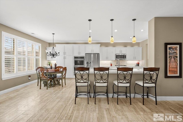 kitchen with appliances with stainless steel finishes, white cabinets, a kitchen breakfast bar, and tasteful backsplash