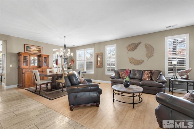 living area with baseboards, visible vents, light wood finished floors, and an inviting chandelier