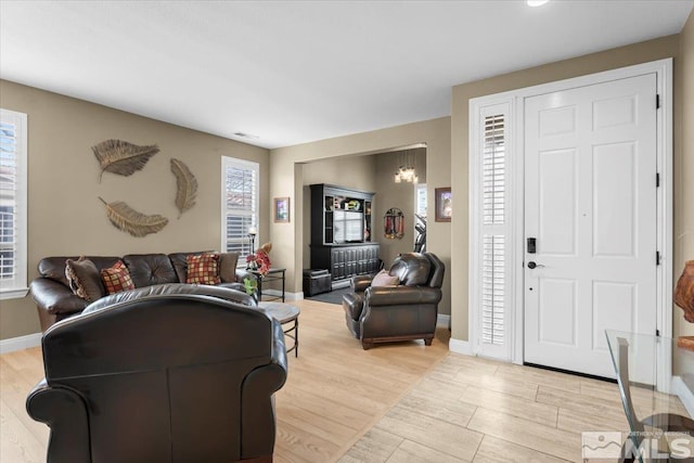 living area featuring light wood-type flooring, visible vents, baseboards, and a notable chandelier