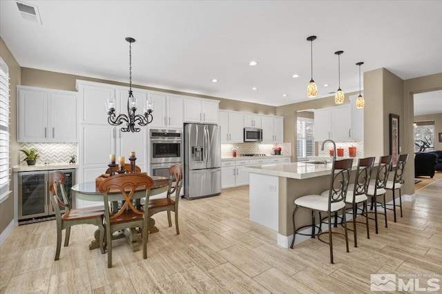 kitchen with appliances with stainless steel finishes, white cabinets, a sink, beverage cooler, and a peninsula