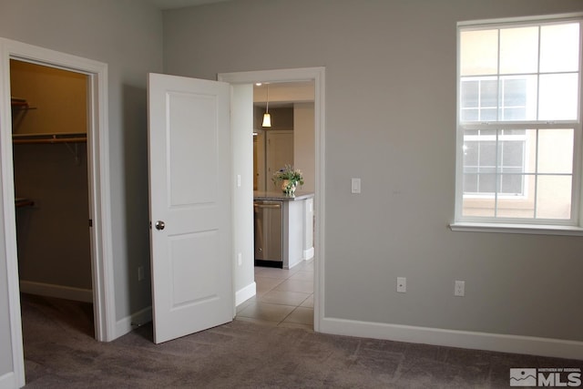 unfurnished bedroom with carpet, a spacious closet, baseboards, and multiple windows