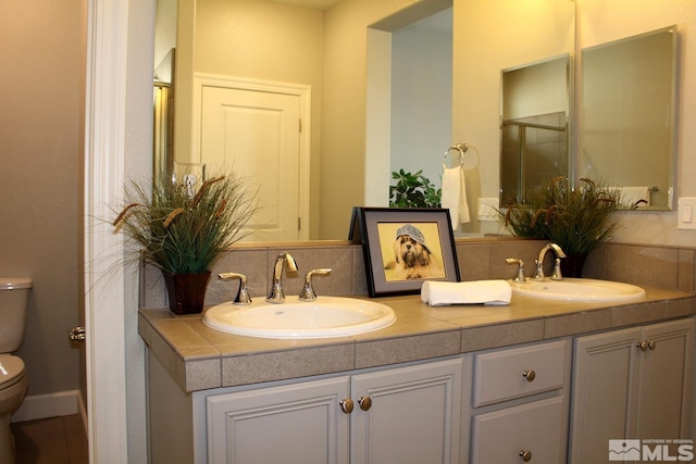 bathroom featuring double vanity, backsplash, a sink, and toilet