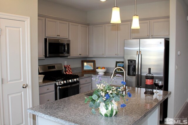 kitchen with a center island with sink, appliances with stainless steel finishes, light stone counters, hanging light fixtures, and a sink