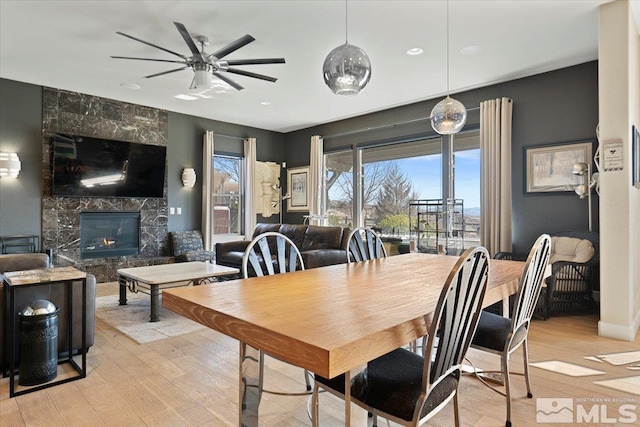 dining room featuring a high end fireplace, ceiling fan, and light wood finished floors