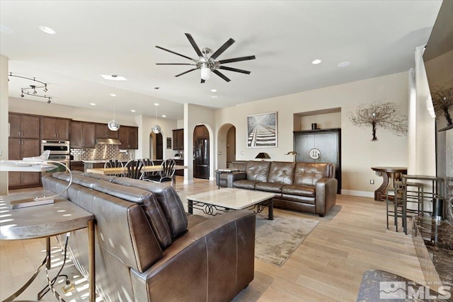 living area with arched walkways, recessed lighting, ceiling fan, light wood-type flooring, and baseboards