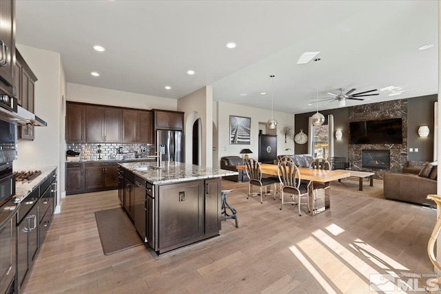 kitchen featuring a large fireplace, arched walkways, appliances with stainless steel finishes, open floor plan, and dark brown cabinets