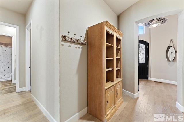 hall featuring light wood-type flooring, baseboards, and arched walkways