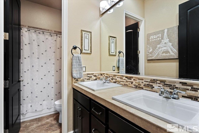 bathroom featuring toilet, tasteful backsplash, double vanity, and a sink