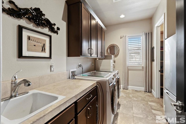 clothes washing area featuring independent washer and dryer, a sink, cabinet space, and baseboards