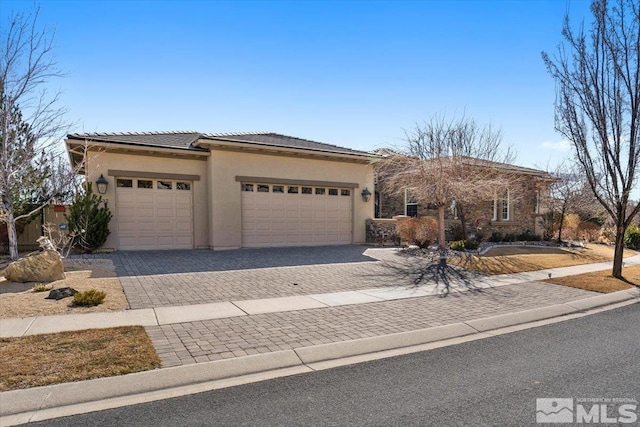 view of front facade featuring a garage, a tiled roof, decorative driveway, and stucco siding