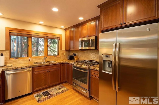 kitchen with light stone counters, brown cabinets, stainless steel appliances, a sink, and light wood-type flooring