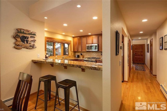 kitchen featuring brown cabinets, light wood finished floors, backsplash, appliances with stainless steel finishes, and a kitchen bar