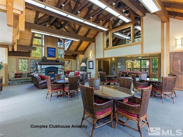 dining space with high vaulted ceiling, a stone fireplace, carpet, and beam ceiling