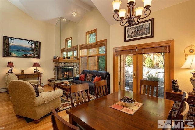 dining area with a notable chandelier, a fireplace, light wood finished floors, baseboard heating, and high vaulted ceiling