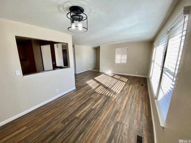 empty room featuring dark wood finished floors, visible vents, and baseboards