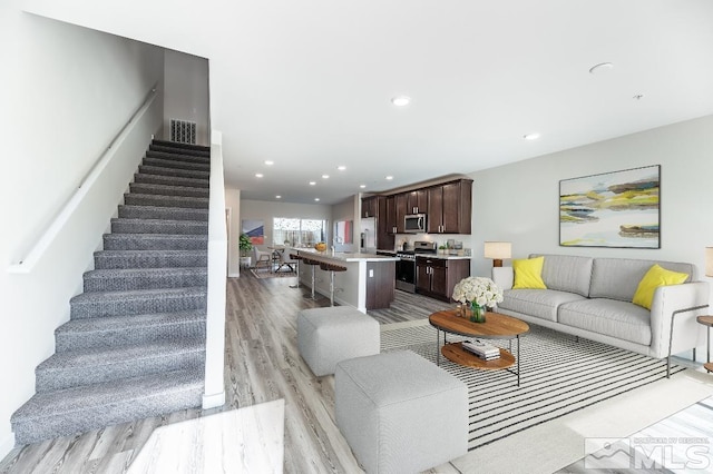 living room featuring light wood finished floors, stairs, visible vents, and recessed lighting